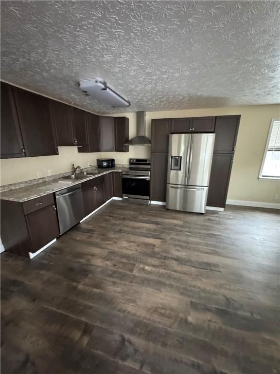 kitchen featuring dark brown cabinetry, dark wood-type flooring, wall chimney range hood, and appliances with stainless steel finishes