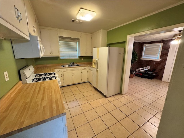 kitchen featuring brick wall, white appliances, sink, light tile patterned floors, and white cabinets