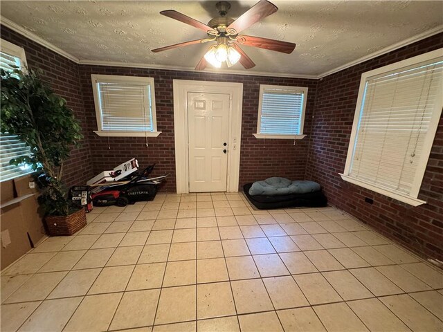 tiled entrance foyer with ceiling fan, crown molding, a textured ceiling, and brick wall