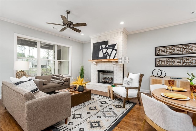 living room featuring ceiling fan, ornamental molding, a brick fireplace, and wood-type flooring
