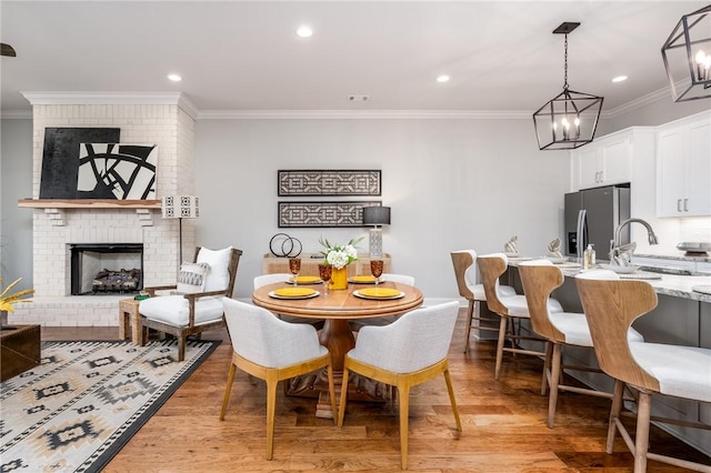 dining room with crown molding, sink, a fireplace, and light hardwood / wood-style flooring