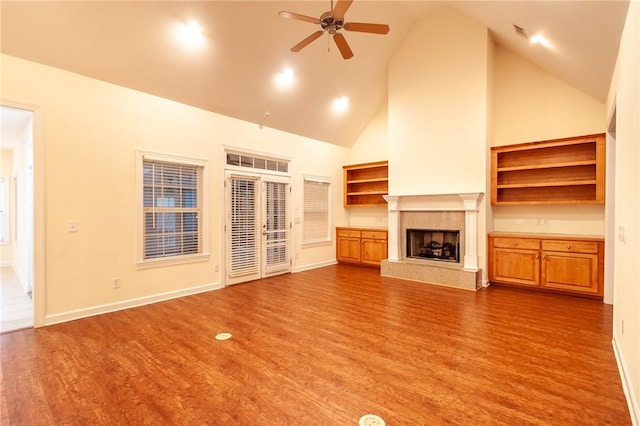 unfurnished living room featuring a tile fireplace, hardwood / wood-style floors, high vaulted ceiling, and ceiling fan