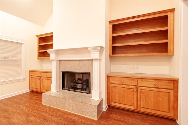 unfurnished living room featuring wood-type flooring, lofted ceiling, and a tile fireplace