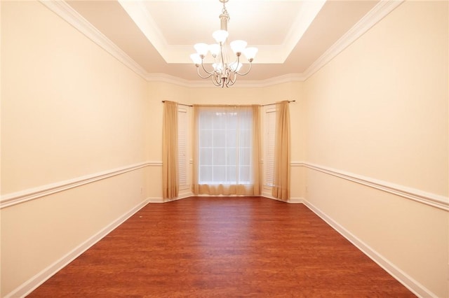 spare room with a raised ceiling, ornamental molding, dark wood-type flooring, and a notable chandelier