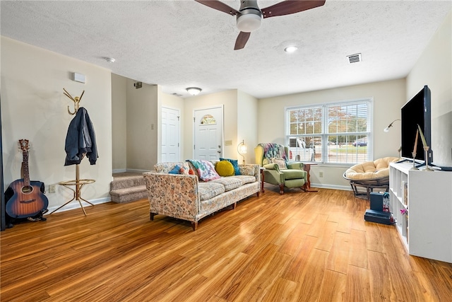 living room with a textured ceiling, light hardwood / wood-style floors, and ceiling fan