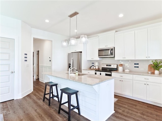 1066 Hunters Way, Opelika, AL 36801 - kitchen featuring appliances with stainless steel finishes, a center island with sink, a kitchen bar, white cabinets, and dark wood finished floors