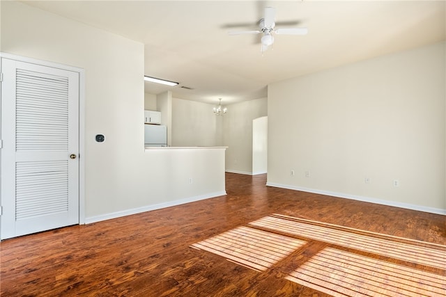 empty room with ceiling fan with notable chandelier, wood finished floors, and baseboards