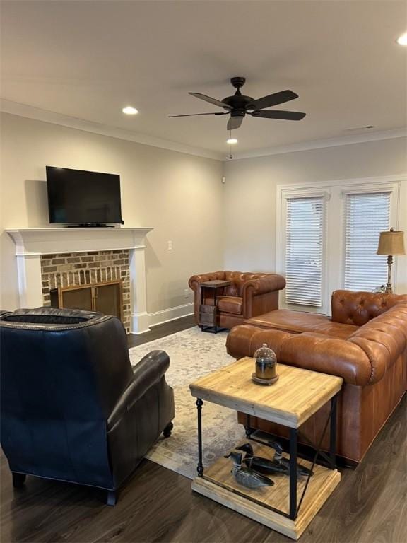 living room featuring ceiling fan, dark hardwood / wood-style flooring, crown molding, and a brick fireplace