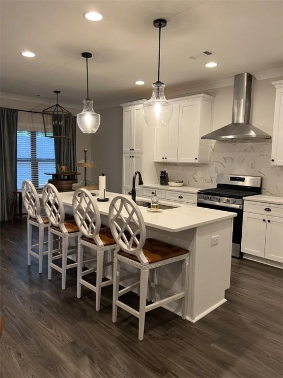 kitchen featuring stainless steel gas stove, wall chimney range hood, dark hardwood / wood-style floors, an island with sink, and white cabinets