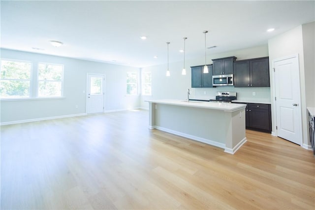 kitchen featuring a kitchen island with sink, hanging light fixtures, stainless steel appliances, light hardwood / wood-style flooring, and decorative backsplash