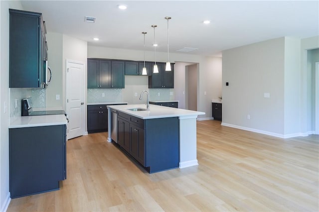 kitchen featuring appliances with stainless steel finishes, sink, decorative light fixtures, light hardwood / wood-style floors, and an island with sink