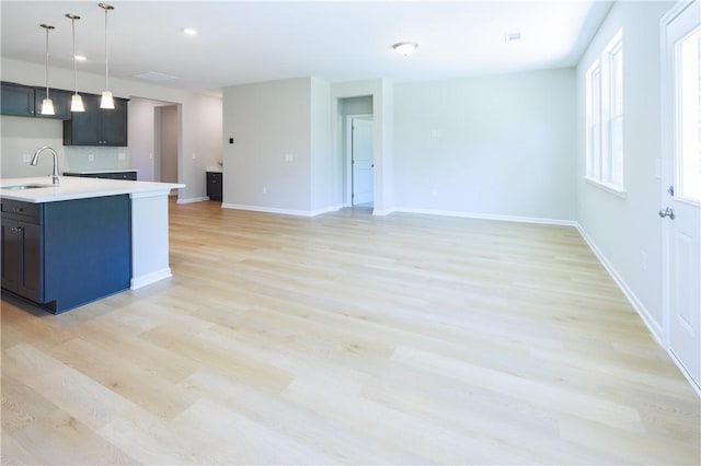 kitchen with backsplash, sink, hanging light fixtures, an island with sink, and light hardwood / wood-style floors