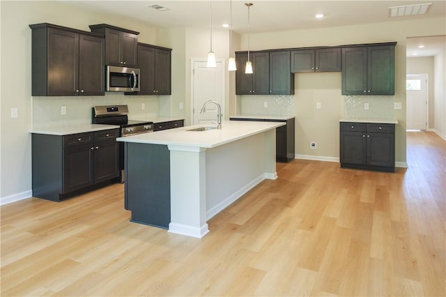 kitchen featuring a center island with sink, sink, hanging light fixtures, light hardwood / wood-style floors, and stainless steel appliances