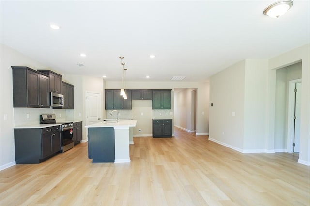 kitchen with backsplash, an island with sink, light hardwood / wood-style floors, pendant lighting, and appliances with stainless steel finishes