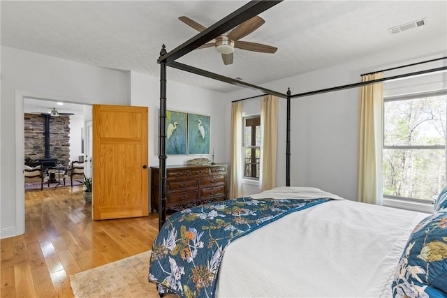 bedroom featuring a ceiling fan, a wood stove, light wood finished floors, and visible vents