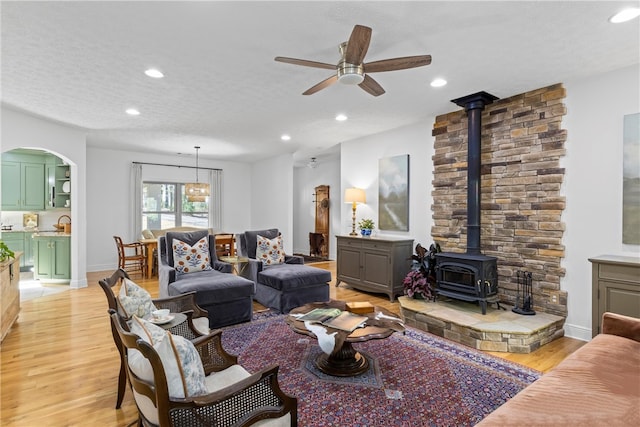 living room featuring light wood-style flooring, recessed lighting, ceiling fan, arched walkways, and a wood stove