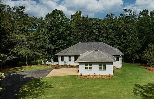 rear view of property with a shingled roof, a yard, driveway, and stucco siding