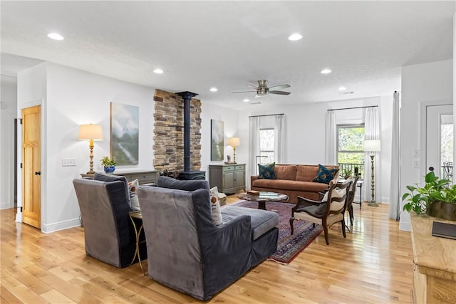 living area featuring a ceiling fan, a wood stove, light wood finished floors, and recessed lighting
