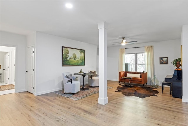 living area featuring light wood-type flooring, baseboards, ceiling fan, and ornate columns
