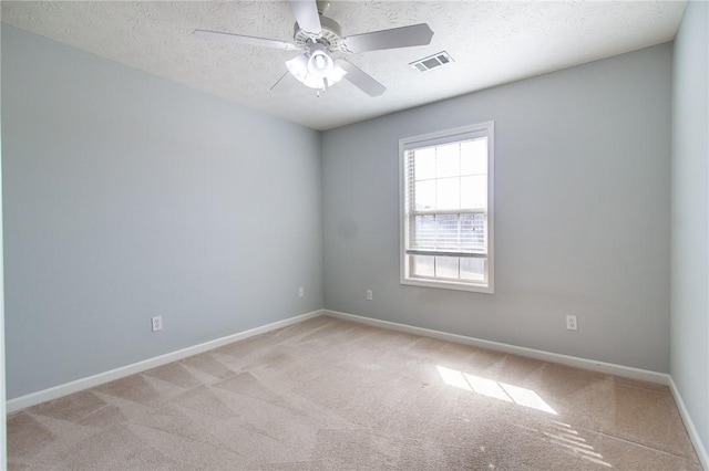 spare room featuring a ceiling fan, visible vents, baseboards, a textured ceiling, and light colored carpet