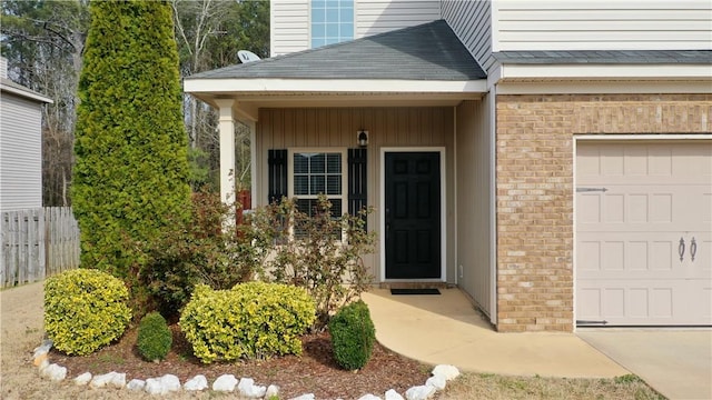 property entrance with brick siding, a shingled roof, an attached garage, and fence