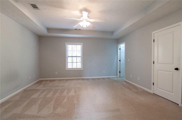 empty room featuring baseboards, visible vents, a raised ceiling, and light carpet