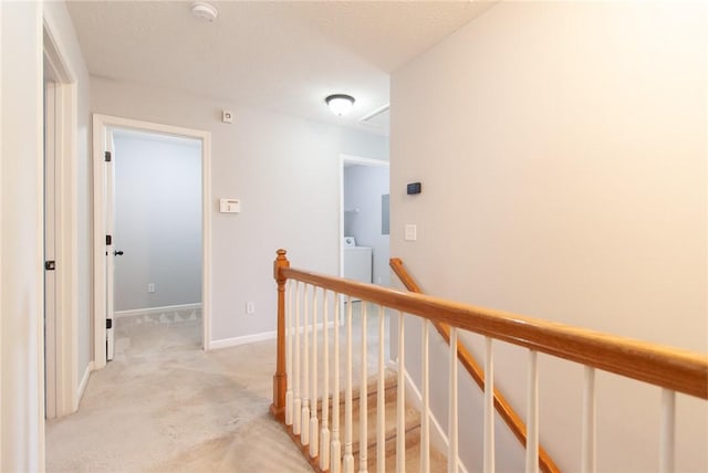 hall with baseboards, light colored carpet, attic access, an upstairs landing, and washer / dryer