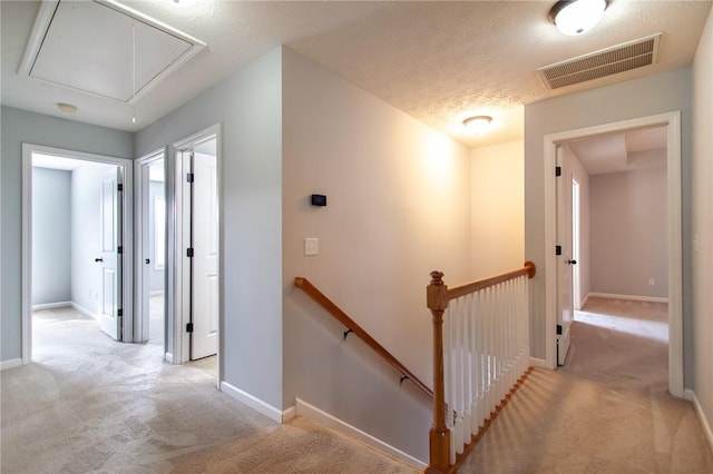 hallway with attic access, an upstairs landing, visible vents, and light carpet