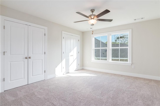 unfurnished bedroom featuring ceiling fan, light colored carpet, and two closets