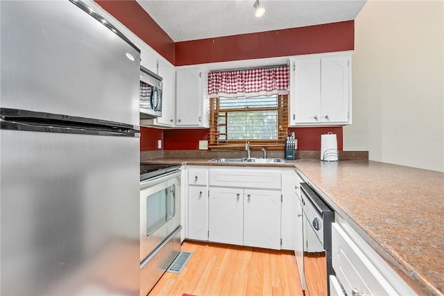 kitchen with sink, appliances with stainless steel finishes, a textured ceiling, white cabinets, and light wood-type flooring