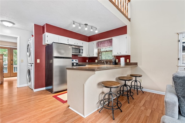 kitchen featuring kitchen peninsula, stacked washer / dryer, appliances with stainless steel finishes, white cabinets, and light wood-type flooring