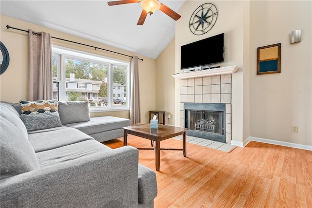 living room with light hardwood / wood-style floors, vaulted ceiling, ceiling fan, and a tiled fireplace