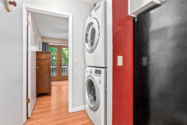 laundry room with french doors, light wood-type flooring, stacked washing maching and dryer, and a textured ceiling