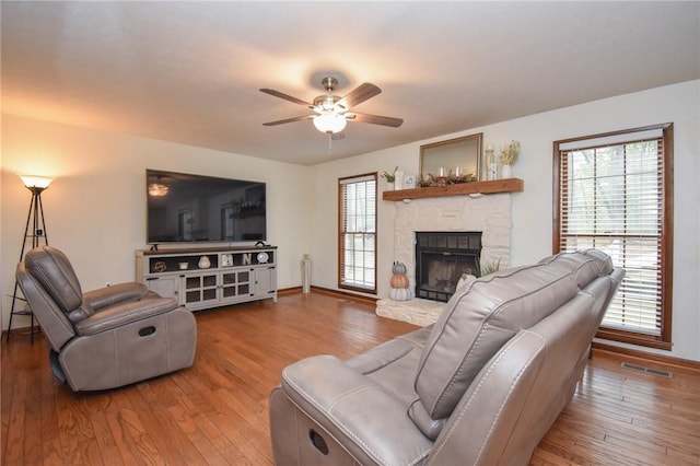 living room with hardwood / wood-style floors, a stone fireplace, and ceiling fan