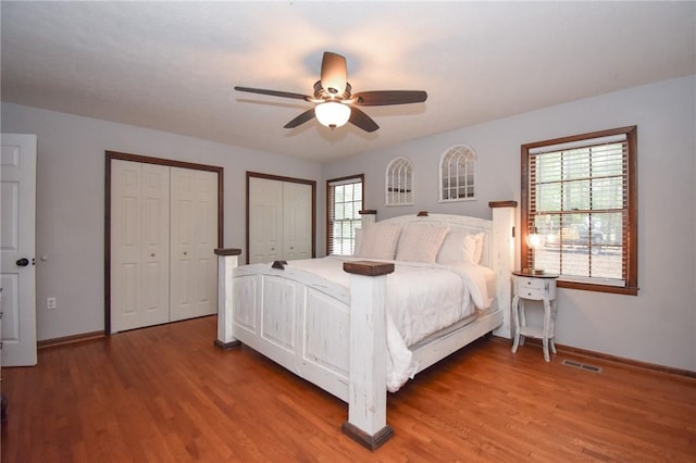 bedroom featuring hardwood / wood-style flooring, ceiling fan, multiple closets, and multiple windows