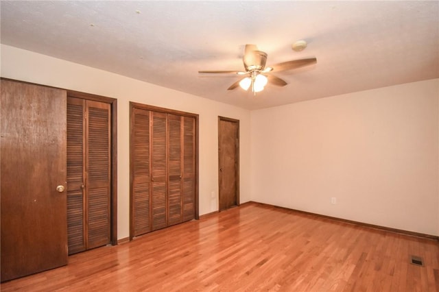 unfurnished bedroom with ceiling fan, two closets, and light wood-type flooring