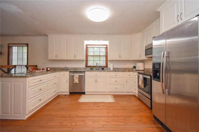 kitchen featuring white cabinetry, sink, stainless steel appliances, kitchen peninsula, and dark stone counters