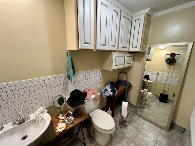 bathroom with ornamental molding, a sink, tile patterned floors, toilet, and tile walls