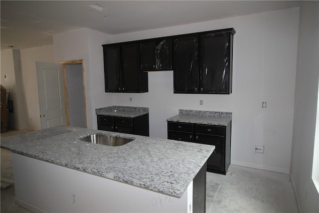 kitchen featuring light stone countertops, baseboards, concrete flooring, and dark cabinets