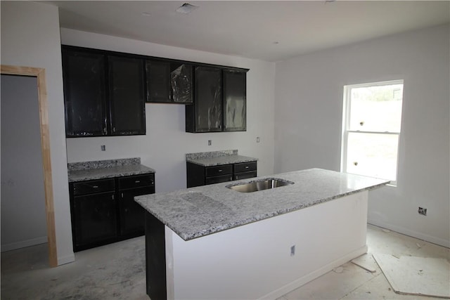 kitchen featuring light stone counters, a sink, visible vents, dark cabinetry, and a center island with sink