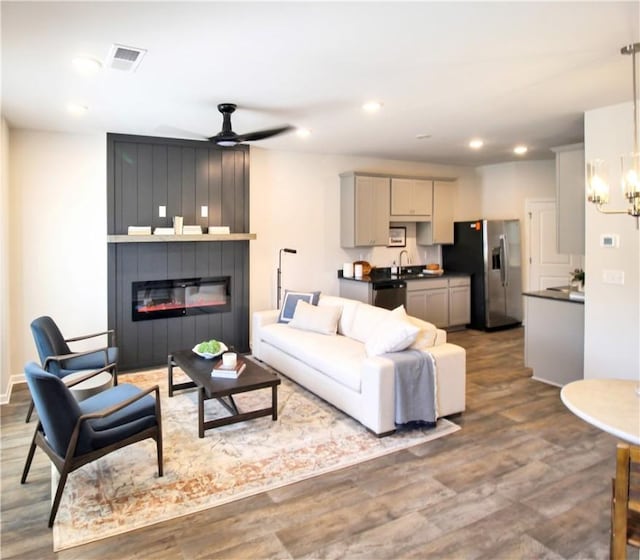 living room featuring visible vents, a large fireplace, recessed lighting, ceiling fan with notable chandelier, and wood finished floors