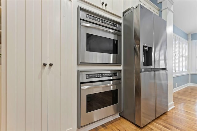 kitchen with white cabinets, stainless steel fridge, light wood-style flooring, and baseboards