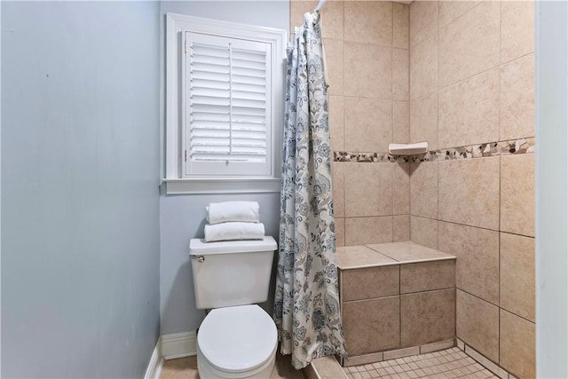 bathroom featuring a tile shower, toilet, and baseboards