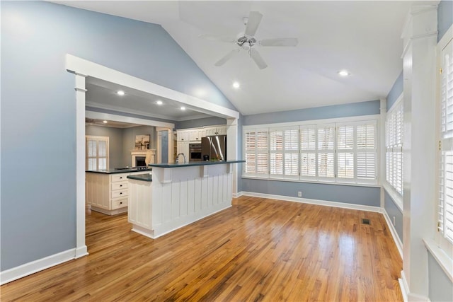kitchen featuring white cabinets, stainless steel appliances, dark countertops, a ceiling fan, and open floor plan