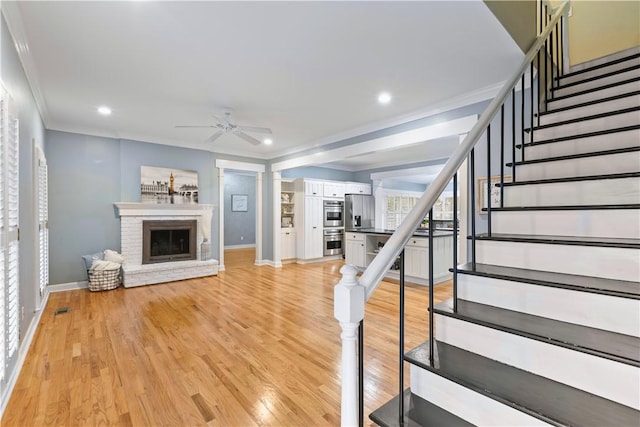 stairs featuring wood finished floors, crown molding, baseboards, a brick fireplace, and ceiling fan