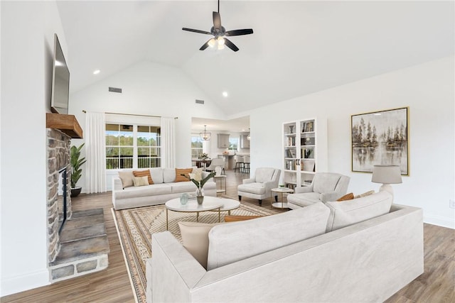 living area with visible vents, high vaulted ceiling, wood finished floors, a stone fireplace, and ceiling fan