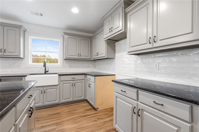 kitchen featuring dark stone countertops, light wood-style flooring, gray cabinets, a sink, and tasteful backsplash
