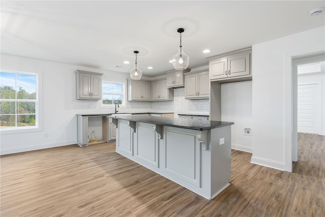 kitchen with baseboards, light wood-style flooring, gray cabinetry, backsplash, and a center island