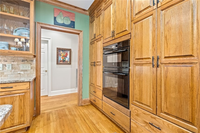 kitchen featuring decorative backsplash, light stone counters, light wood-type flooring, and double oven