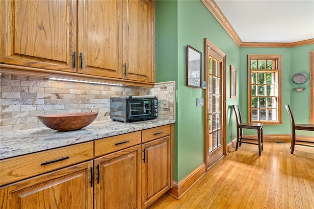 kitchen featuring decorative backsplash, light hardwood / wood-style flooring, light stone counters, and ornamental molding